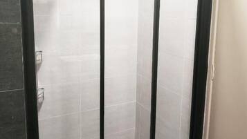 A shower area with tiled walls and floor, a black door frame, and a visible hand soap dispenser.