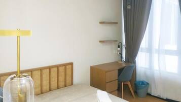 Een hotelkamer met een bed, een bureau, een stoel, een lamp, een prullenbak en een raam met gordijnen.