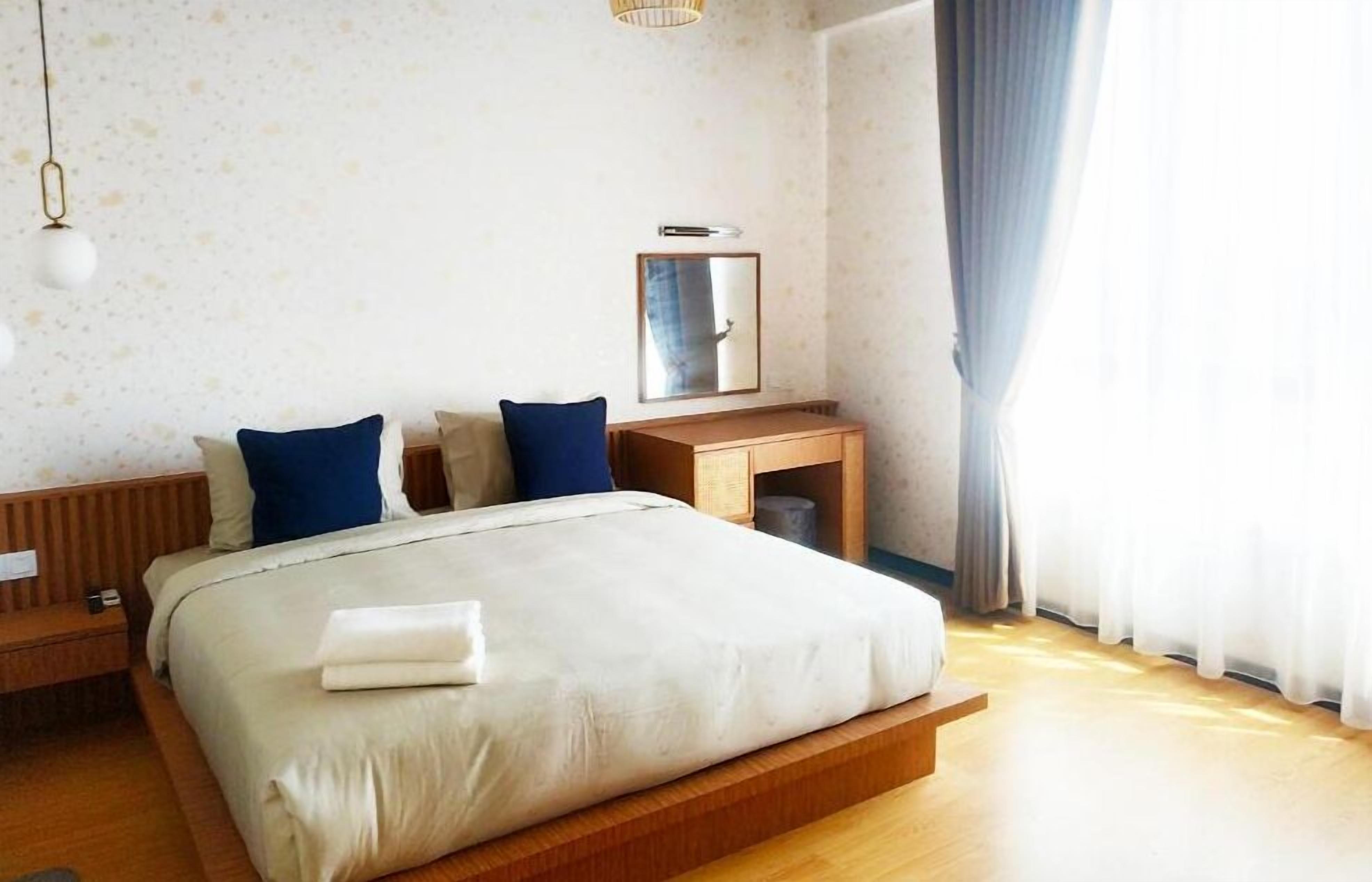 A neatly made bed with a wooden headboard, a bedside table, and a mirror above it.