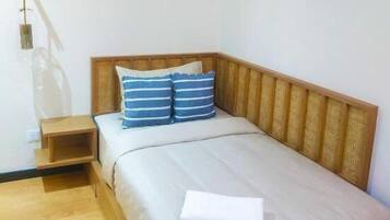 Una cama individual con cabecera de madera, dos almohadas, una mesita de noche y una lámpara.