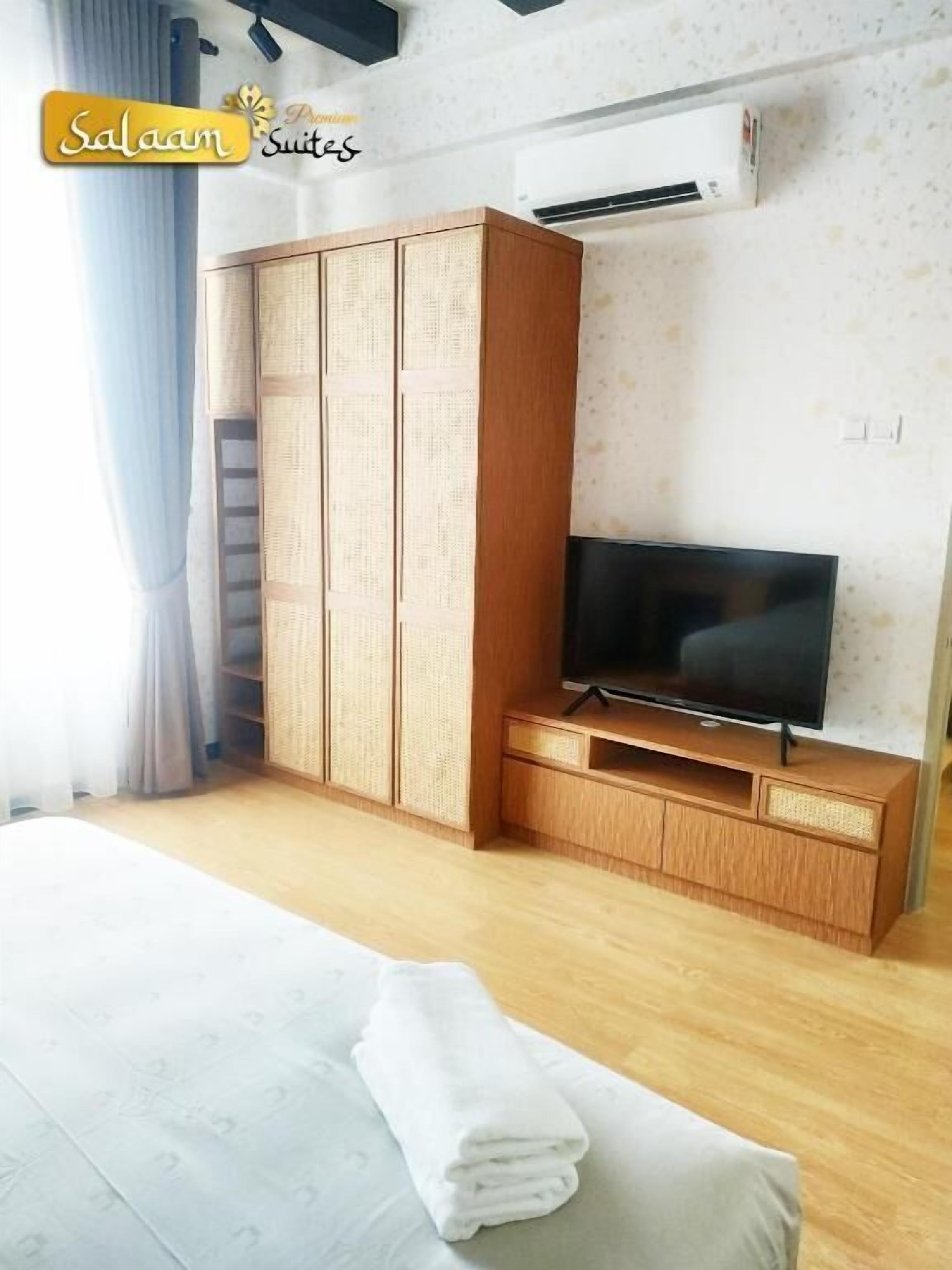 Habitación de hotel con cama, televisión sobre un soporte de madera, armario con motivo tejido y unidad de aire acondicionado en la pared.