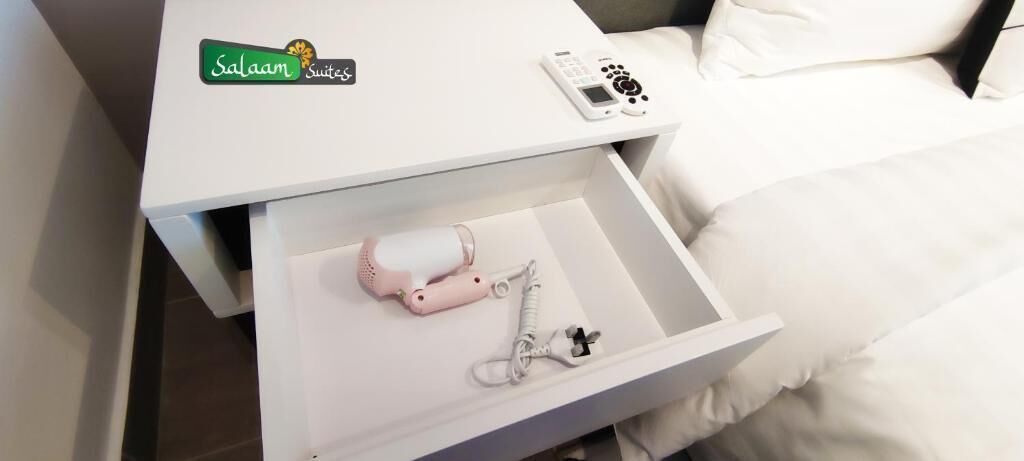 Un comodino bianco con un piccolo cassetto che contiene una tettarella rosa e un paio di scarpine per neonato.