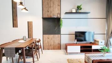 A modern living room with a wooden dining table, chairs, a TV on a wooden stand, and a plant on the shelf.