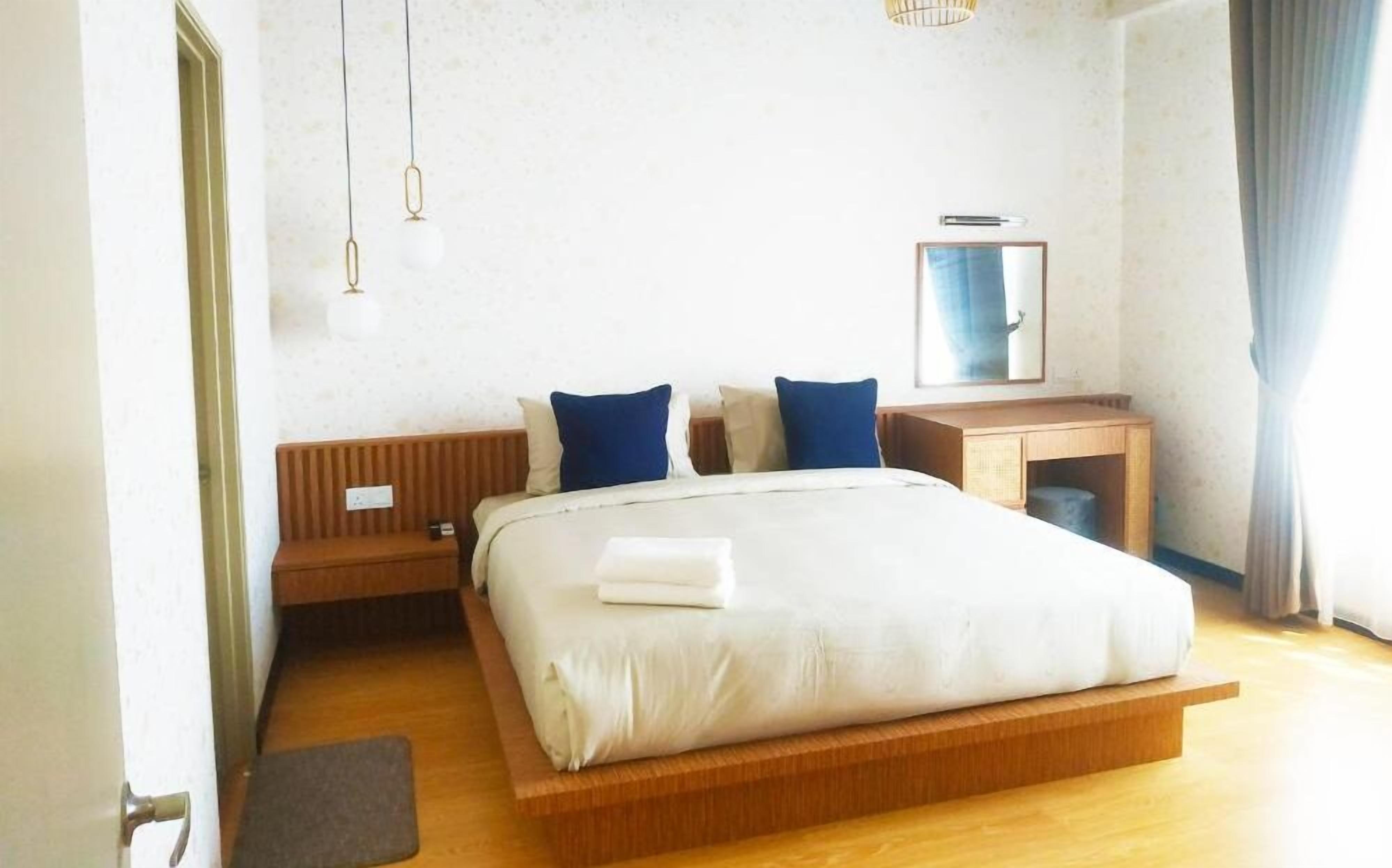 A modern hotel room with a wooden bed, a bedside table, a mirror, and a desk.