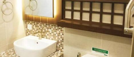 A bathroom with a white sink, a toilet, and a window above the toilet. There are three potted plants on a shelf above the window.