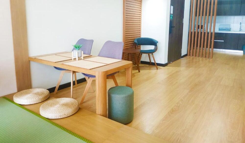 Una stanza con un tavolo da pranzo in legno, due sedie, una piccola pianta e un tappetino verde sul pavimento.