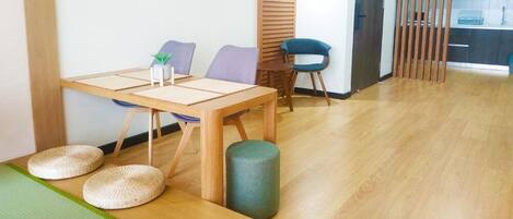 Una stanza con un tavolo da pranzo in legno, due sedie, una piccola pianta e un tappetino verde sul pavimento.