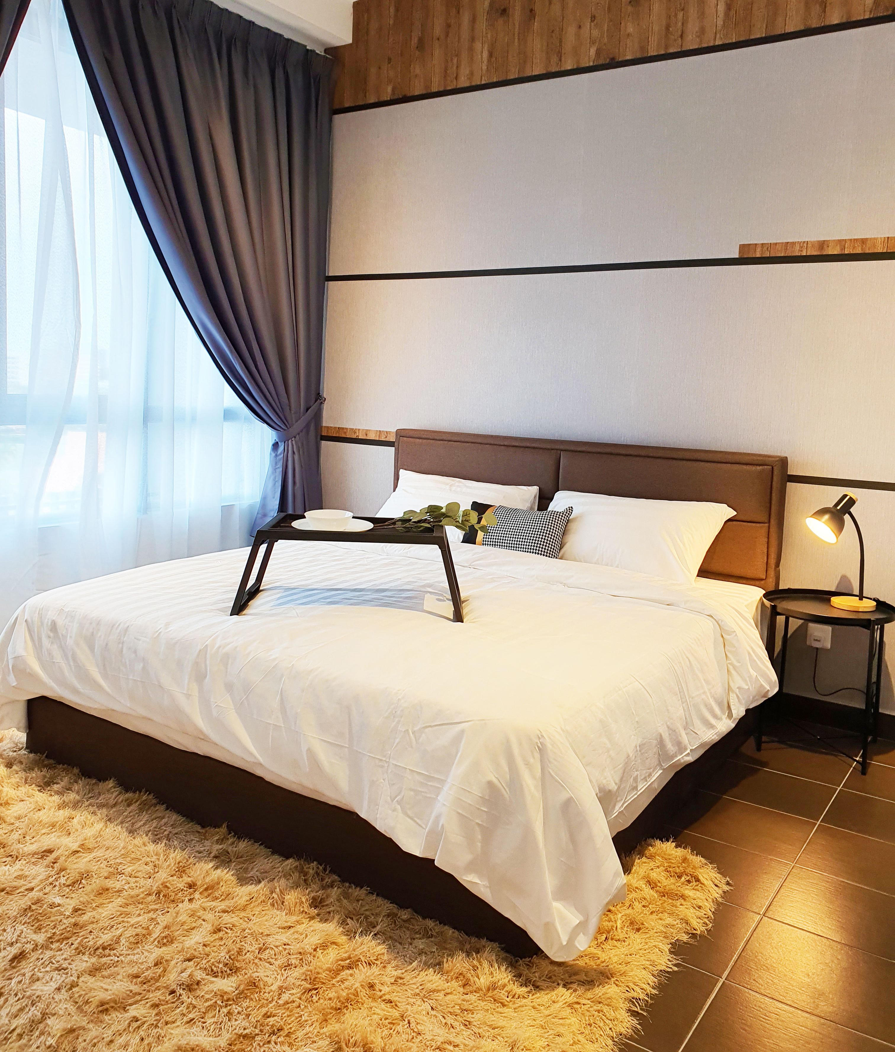 A hotel room with a bed, a nightstand, a lamp, a tray with a plant, and a window with curtains.