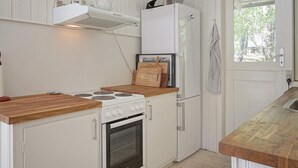 A compact kitchen with a stove, oven, and refrigerator, wooden countertops, and a window with a view of greenery. - 7 Person Holiday Home in Nexo (Nexø)