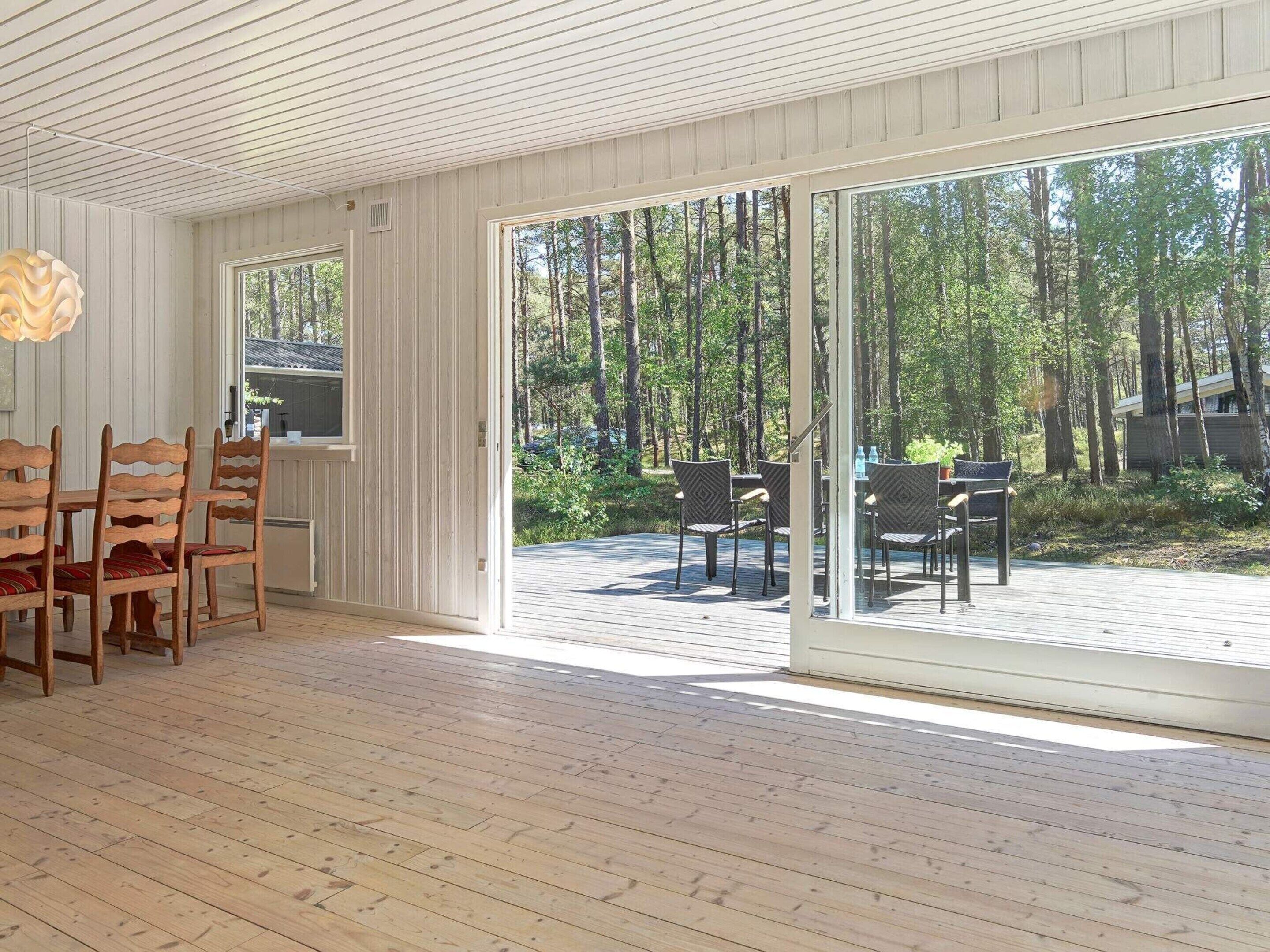Una habitación amplia con un gran ventanal corredero que da a una terraza exterior. En el interior, hay una mesa de madera con sillas y un banco.