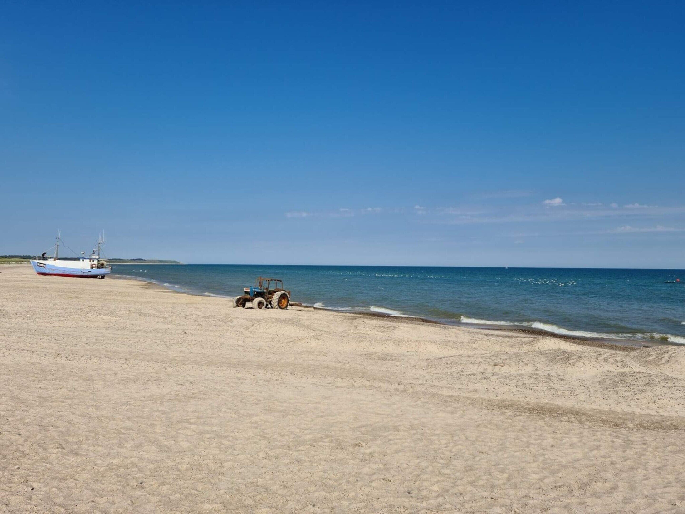 A beach with a fishing boat and a tractor on the sand.