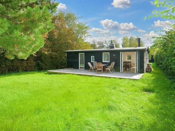 A modern house with a deck, a dining area with chairs, and a large window.