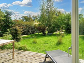 A wooden deck with a metal chair and a table, overlooking a lush garden with various trees and shrubs. - 6 Person Holiday Home in Gilleleje (Gilleleje)