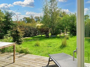 A wooden deck with a metal chair, overlooking a lush green garden with various trees and shrubs.