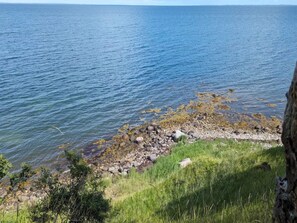 A coastal landscape with a rocky shoreline, clear blue water, and greenery. - 4 Person Holiday Home in Bogense (Bogense)