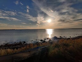 Un atardecer sobre una masa de agua tranquila, con una costa rocosa y vegetación escasa.
