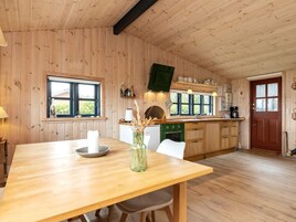 A wooden interior with a dining table, chairs, a kitchen with a stove, and a window.