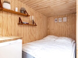 A bedroom with a wooden ceiling, a bed with white bedding, a small bedside table, and a shelf with decorative items.