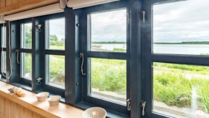 A room with large windows overlooking a body of water, a wooden ceiling, and a shelf with bowls. - 4 Person Holiday Home in Bogense (Bogense)