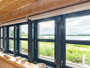Una habitación con amplios ventanales con vistas a un cuerpo de agua, techo de madera y una repisa con cuencos.