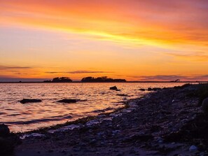 Un atardecer sobre una costa rocosa con agua tranquila y formas de tierra en la distancia.