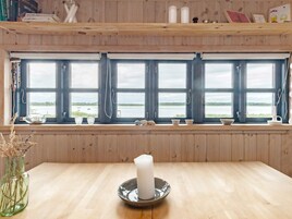 Una habitación con interiores de madera, un ventanal con múltiples vidrios, una mesa con una vela y varios objetos decorativos en el alféizar.