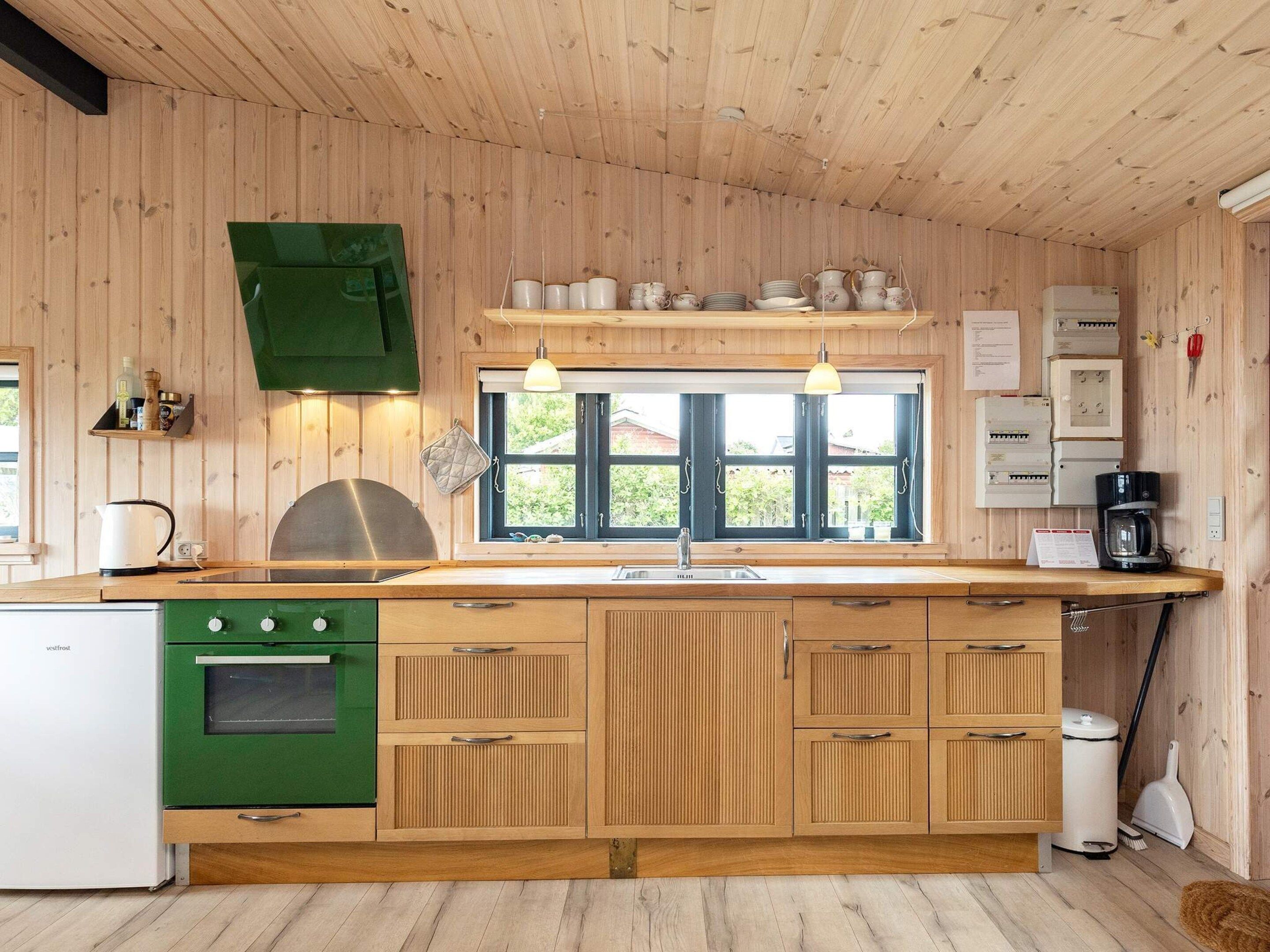 A kitchen with wooden cabinets, a green stove, a window with blinds, and a coffee maker.