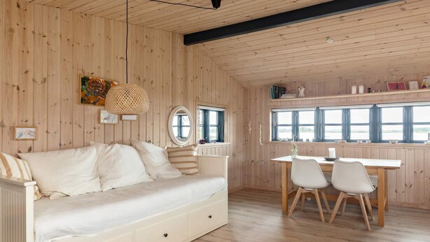 A wooden interior with a sofa, a dining table with chairs, a hanging light fixture, and a window with curtains. - 4 Person Holiday Home in Bogense (Bogense)
