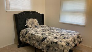Une chambre à coucher avec un lit, une tête de lit et deux fenêtres équipées de stores.