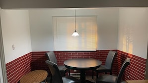 Une pièce d’angle avec une table ronde, quatre chaises, une petite table en bois et une fenêtre avec des stores.
