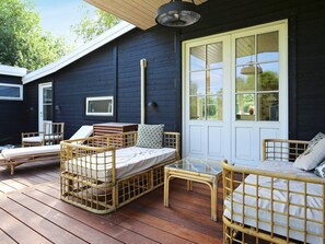A wooden deck with wicker furniture, including a bed and chairs, and a large window with a view of greenery. - 4 Star Holiday Home in Vejby (Vejby)
