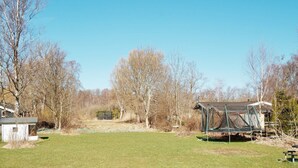 A grassy yard with a small shed, a trampoline, and leafless trees. - 4 Star Holiday Home in Vejby (Vejby)