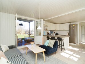 Uma sala de estar moderna com sofá, mesa de jantar e cozinha equipada com armários brancos e geladeira de aço inoxidável.