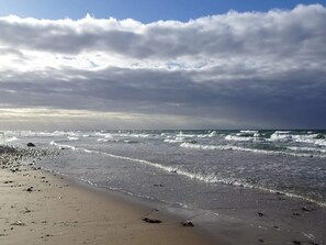Uma praia com ondas, um cais ao longe e um céu nublado.