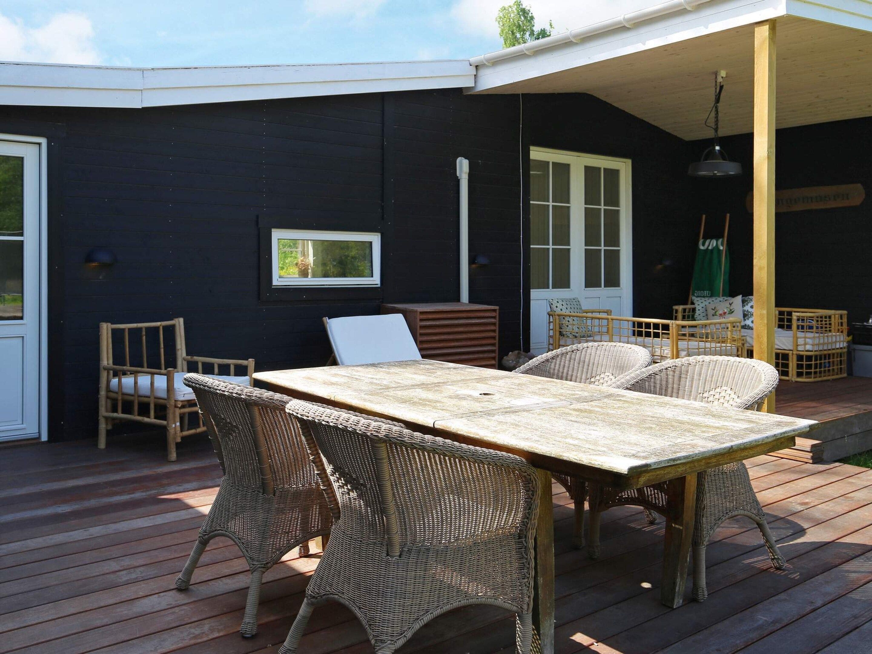 A covered outdoor patio with a table and wicker chairs, a door, and a window.