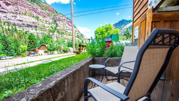 A balcony with a chair and table overlooking a mountainous area with a road and buildings. - Walk to Downtown! 2-bedroom with mountain views (Ouray)
