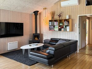 A modern living room with a black leather sofa, a white coffee table, a fireplace, a bookshelf, and a flat-screen TV mounted on the wall.