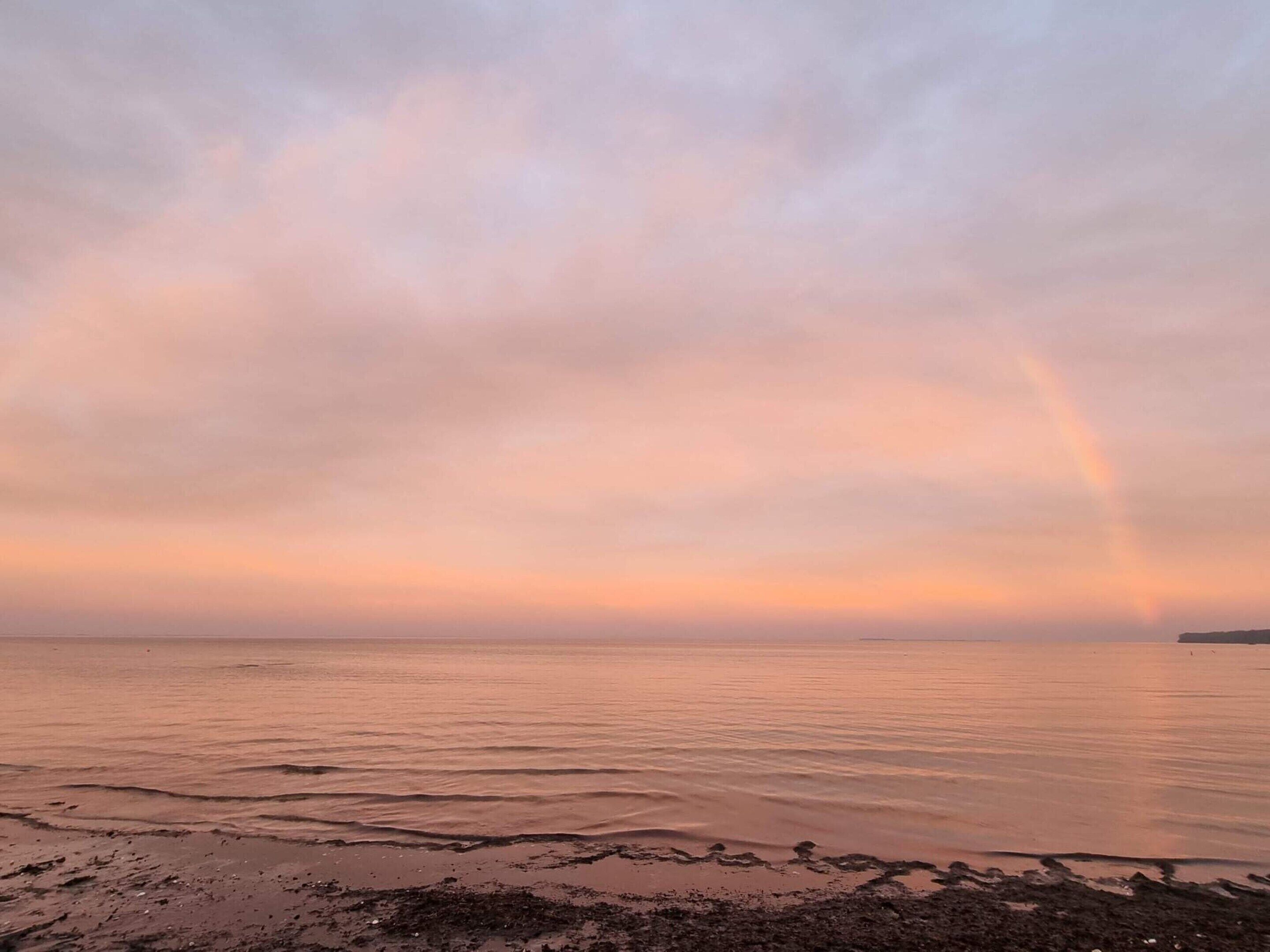 A beach with a calm sea and a rainbow in the sky.