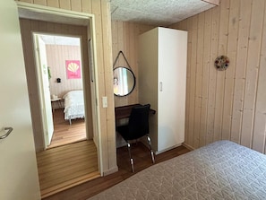 A bedroom with a bed, a desk, a chair, a wardrobe, a mirror, and a door leading to another room. - 4 Star Holiday Home in Bjert (Bjert)