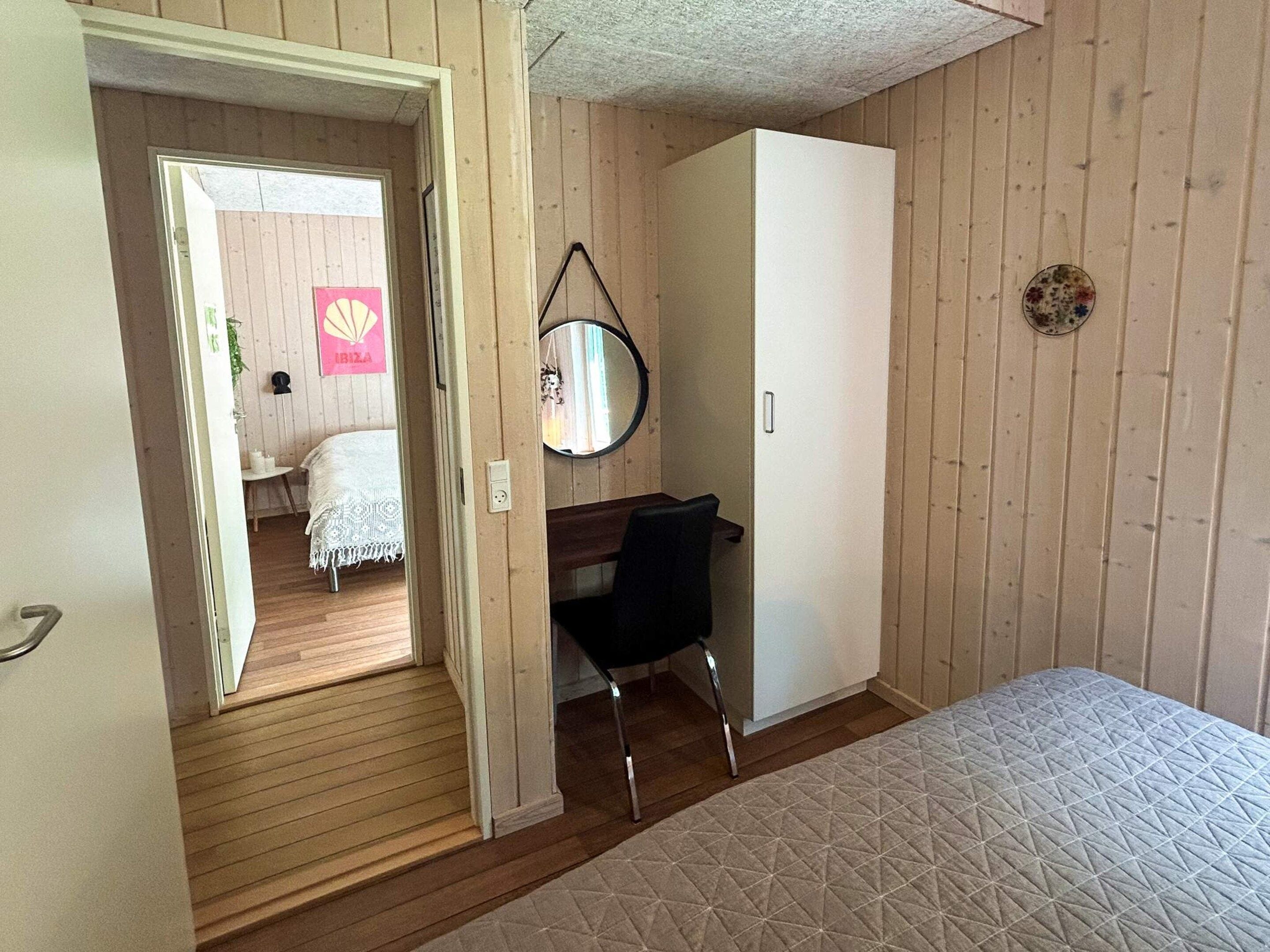 A bedroom with a bed, a desk, a chair, a wardrobe, and a mirror.
