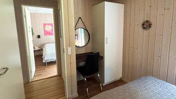 A bedroom with a bed, a desk, a chair, a wardrobe, and a mirror.