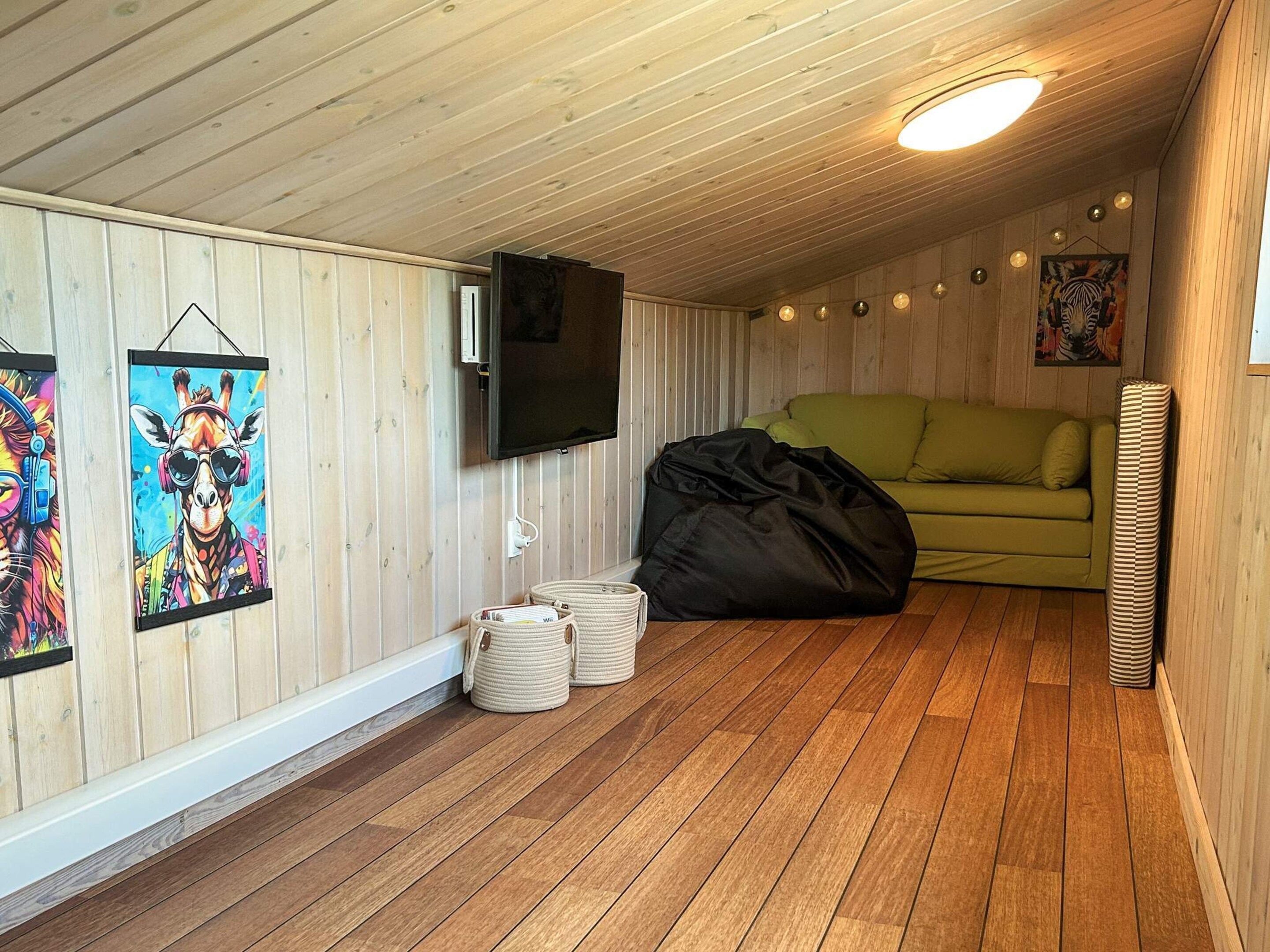 A room with wooden walls, a green sofa, a flat-screen TV, and two wall-mounted paintings.