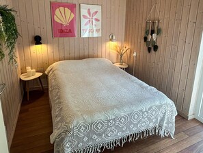 A bedroom with a white knitted bedspread, wooden walls, a small bedside table with candles, and wall art depicting Ibiza and Tuscany. - 4 Star Holiday Home in Bjert (Bjert)