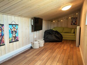 A room with wooden walls, a green sofa, a flat-screen TV, and two wall-mounted paintings. - 4 Star Holiday Home in Bjert (Bjert)