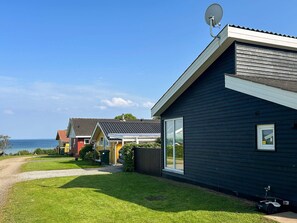 A modern house with a satellite dish, large windows, and a view of the sea.