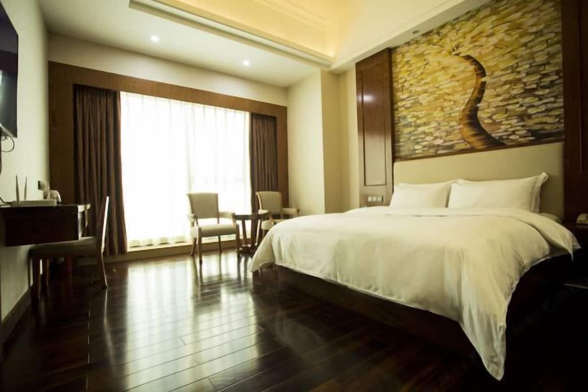 Habitación de hotel con una cama grande, un escritorio, una silla y vistas al exterior a través de una ventana con cortinas.