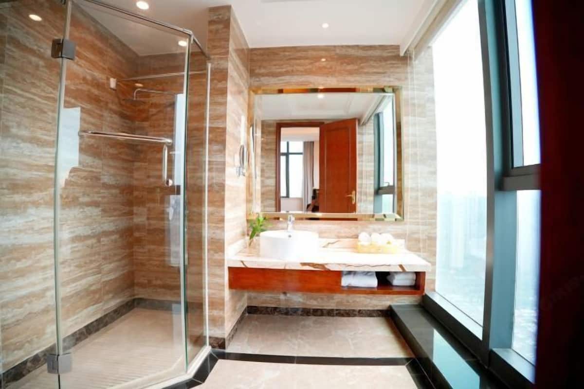 Un baño moderno con cabina de ducha de vidrio, tocador con espejo y un ventanal grande.