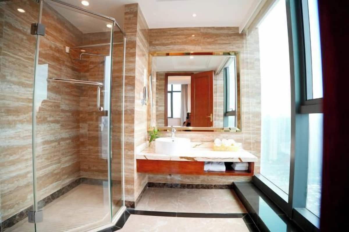 Un baño moderno con cabina de ducha de vidrio, tocador con espejo y un amplio ventanal.