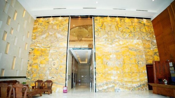 Un hall d’entrée doté d’un sol en marbre, de meubles en bois et d’un grand mur orné d’un motif jaune et doré.