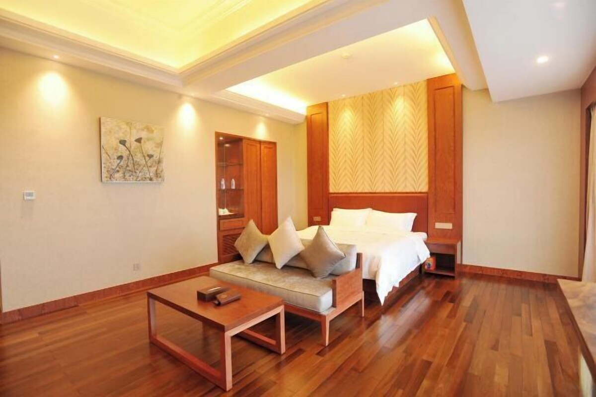 A modern hotel room with a wooden floor, a sofa with cushions, a bed with white linens, and a painting on the wall.